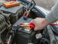 Ręka podłącza kable rozruchowe do akumulatora samochodowego.