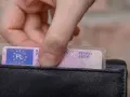 Dłoń wkłada polskie prawo jazdy do czarnego portfela.