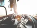 Widok z kabiny kierowcy ciężarówki na kierownicę i deskę rozdzielczą w słońcu.