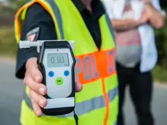 Policjant w kamizelce odblaskowej trzyma alkomat z wynikiem 0.93 promila.