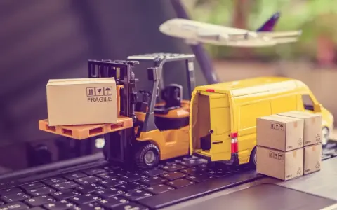 Miniaturki: wózek widłowy z paczką, żółta furgonetka, samolot i pudełka na klawiaturze.