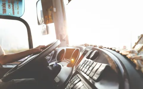 Widok z kabiny kierowcy ciężarówki na kierownicę i deskę rozdzielczą w słońcu.