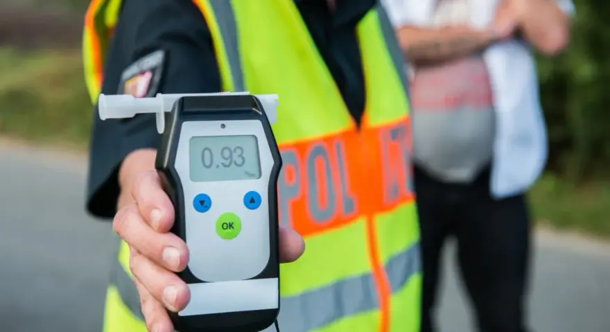 Policjant w kamizelce odblaskowej trzyma alkomat z wynikiem 0.93 promila.